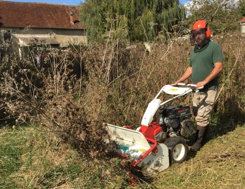Artisan équipé d'un casque de sécurité utilisant une débroussailleuse à roues professionnelle (broyage de ronces) pour nettoyer un terrain en friche à Lescar.
